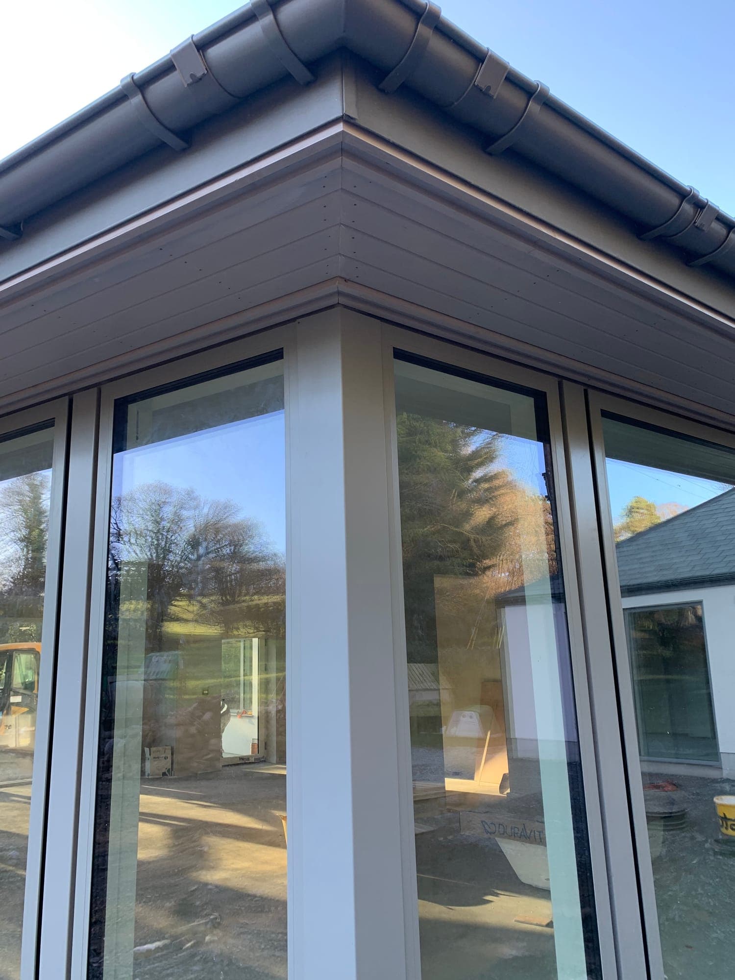 Close-up of a slim aluminium corner glazing junction under a clean soffit against blue sky, by MDM Windows & Doors