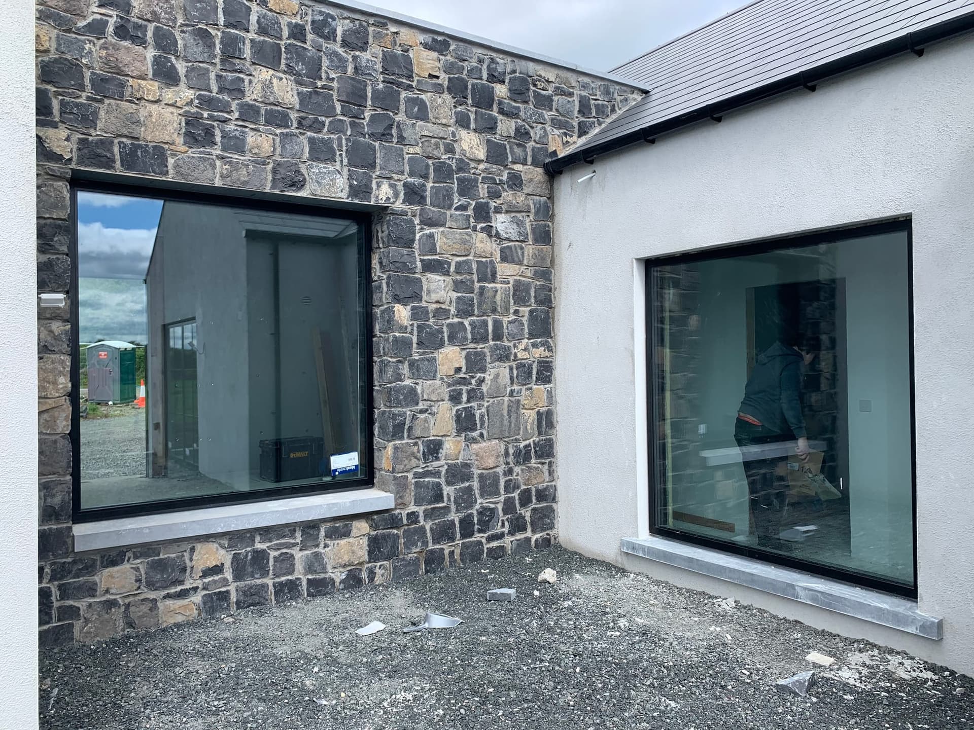 Black-framed picture windows wrapping a stone and rendered corner, by MDM Windows & Doors