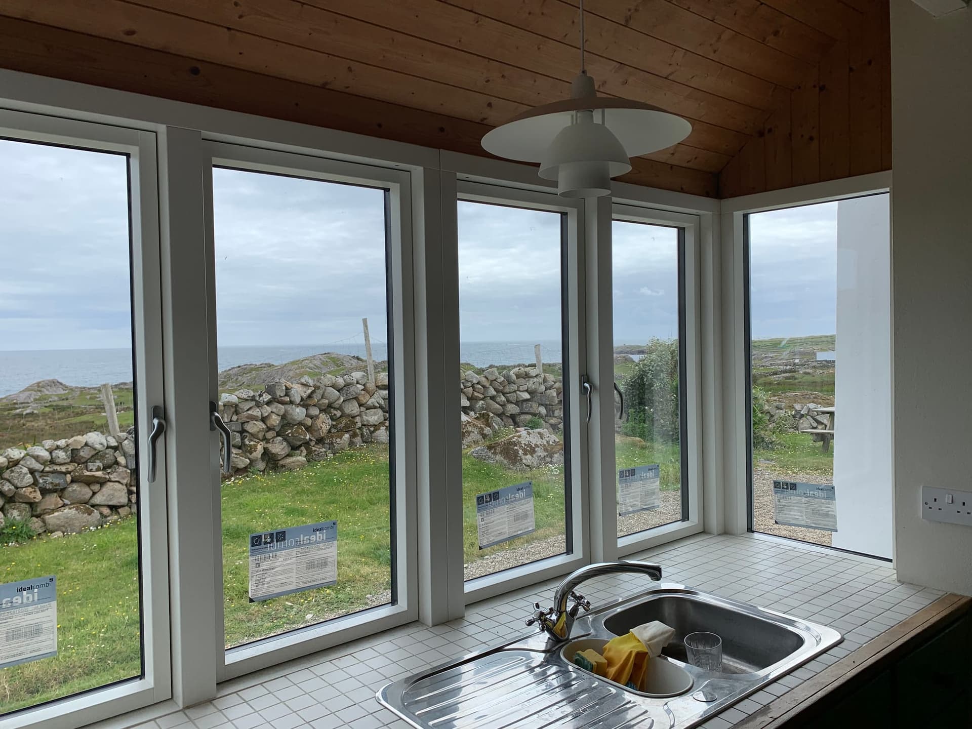 Bright kitchen with white-framed corner windows and doors framing a coastal sea view, fitted by MDM Windows & Doors