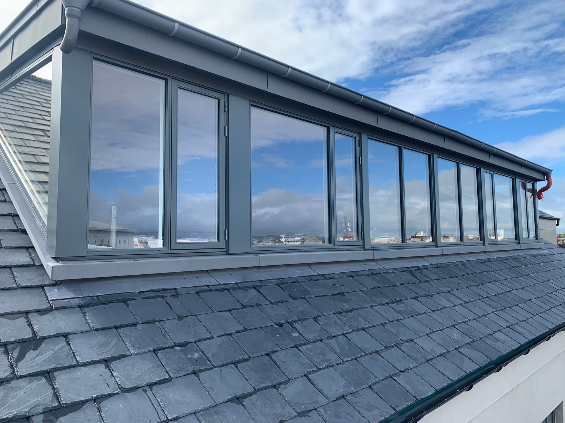 Long run of anthracite aluminium windows on a slate-roofed rooftop development overlooking the coast, by MDM Windows & Doors